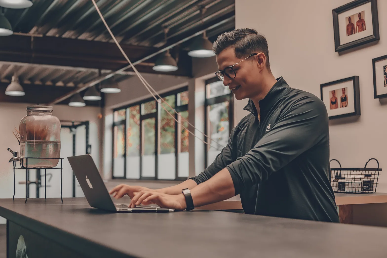 Smiling man standing at a counter working on his laptop in a gym.